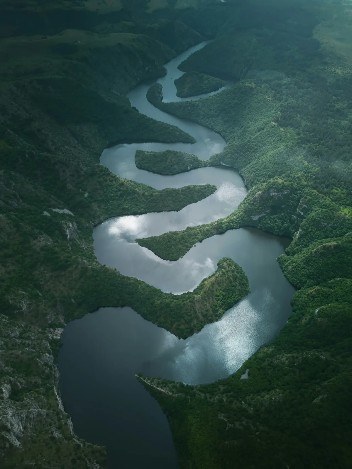 Winding mountain river seen from above, surrounded by lush green hills